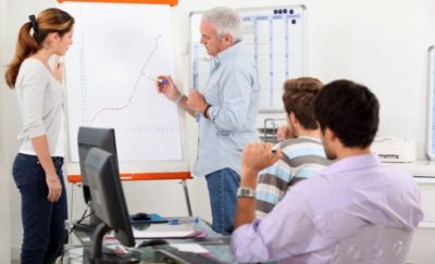 a photo of a teacher in front of a white chart training three students undergoing alternative education programs how to correctly make a graph
