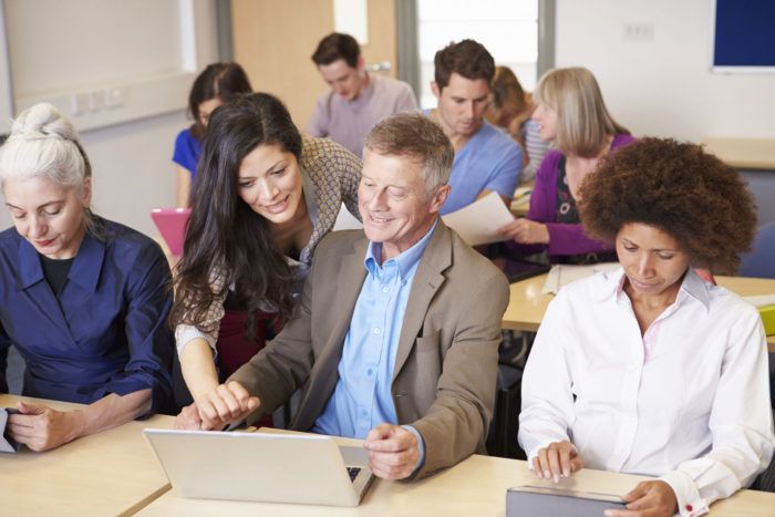 group of adults working together on digital topics in a classroom to overcome the causes of digital divide
