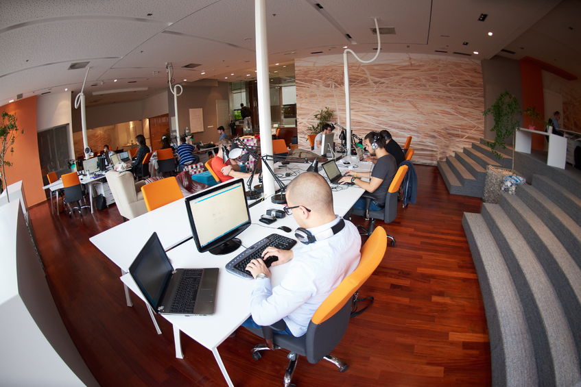 a photo with a fish's eye view of an open office with a white male in a polo (at the center of the image)working in front of a computer that tells him the current data on EverFi investing situation