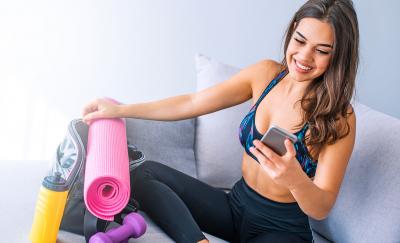a woman wearing a workout outfit sitting with her exercise tools and looking at apps for female health on her smartphone