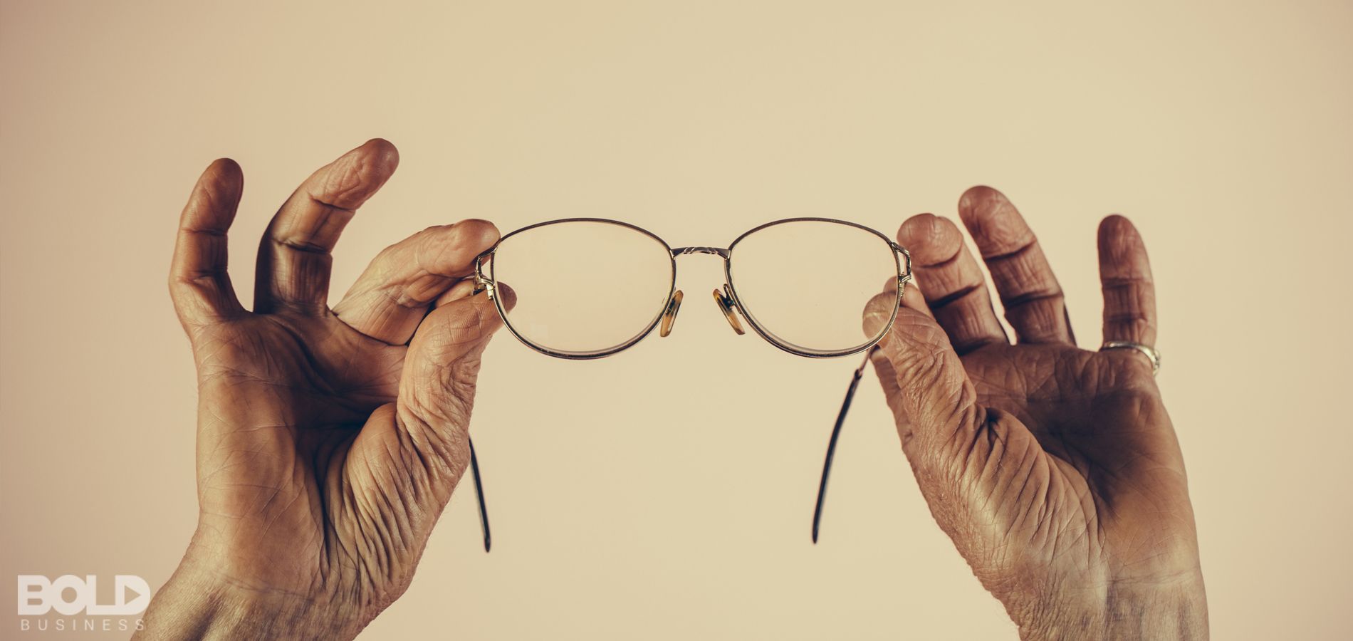 An elderly person holding up a pair of glasses